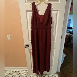 Burgundy jumpsuit with deep V-neck, tailored waist, and wide-leg elegant design.